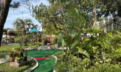 A long hole on a miniature golf course with green foliage along on side