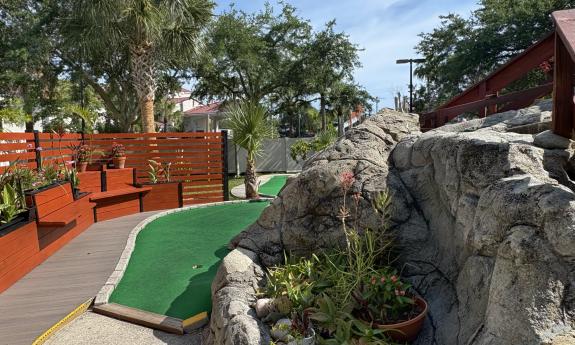 A hole in a miniature golf course with a rock wall on one side and seating on the other