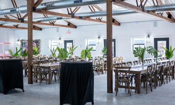 The interior of the Cypress Barn with a few hightops and several long farmers'-style tables decorated for an event