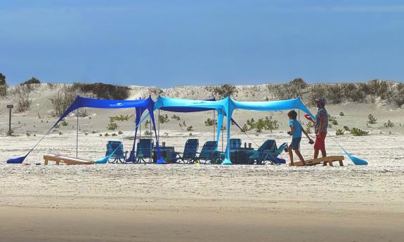 A full setup with a cabana, chairs, and a cornhole game