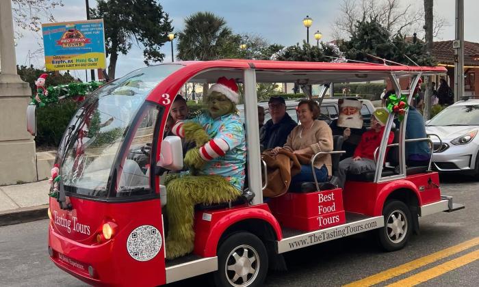 A three-row electric vehicle with passengers, driven by a Grinch for a holiday tour