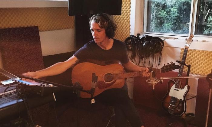 A musician seated in th ecorner of a living room, with musical equipment in an arc around him