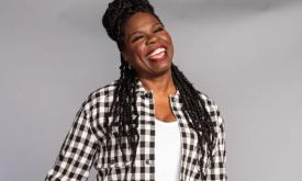 Comedian Leslie Jones smiles in front of a grey backdrop. 