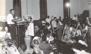 B&W Dr. MLK Jr. stands at a podium at St. Paul SME Church, speaking to a group of supporters.