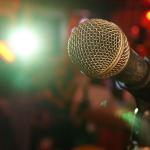 Comedians face a microphone, lights, and an audience seeking laughter. 