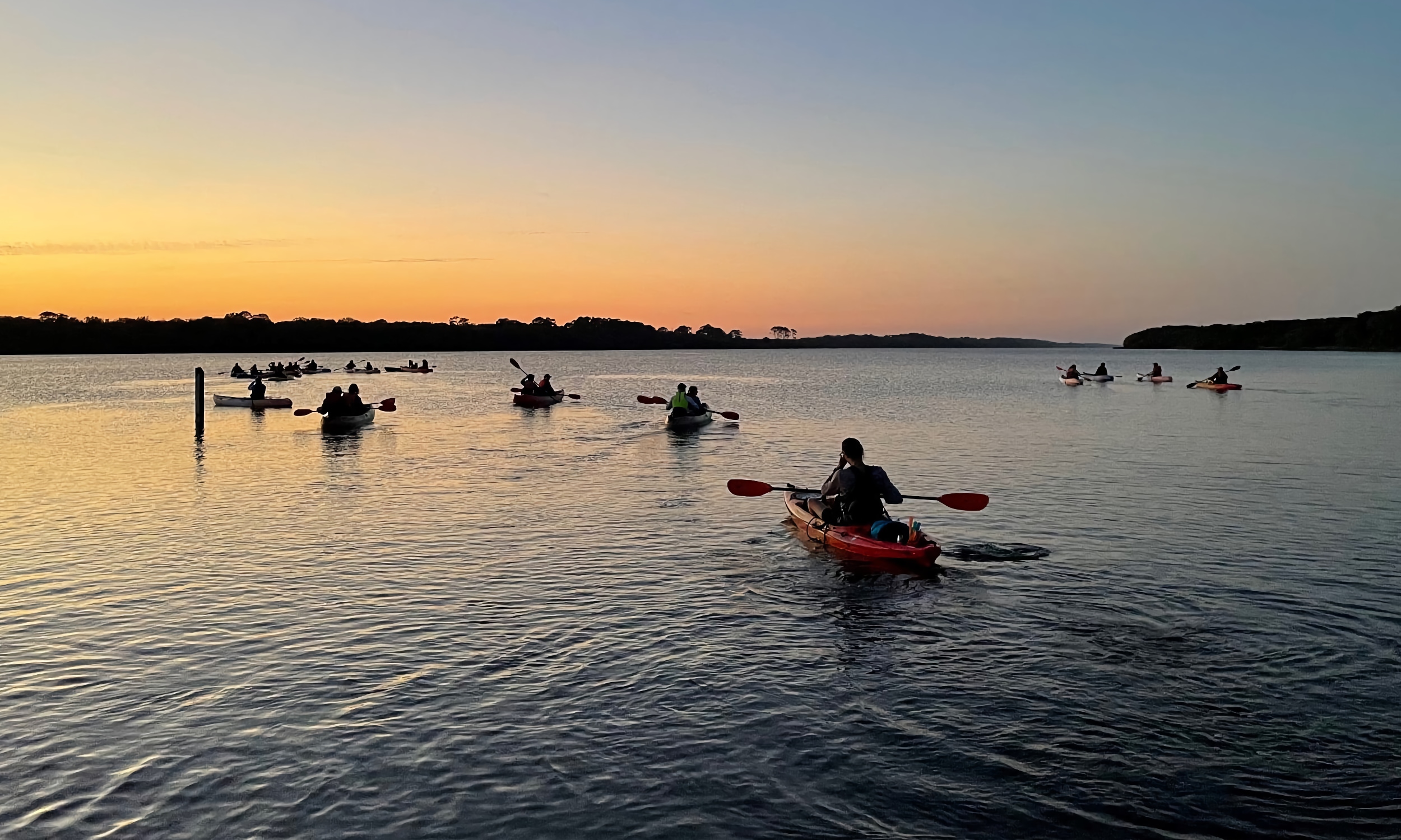 People paddling kayaks toward the sunset in Guana
