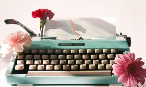 A green typewriter is positioned in front of a pink backdrop.