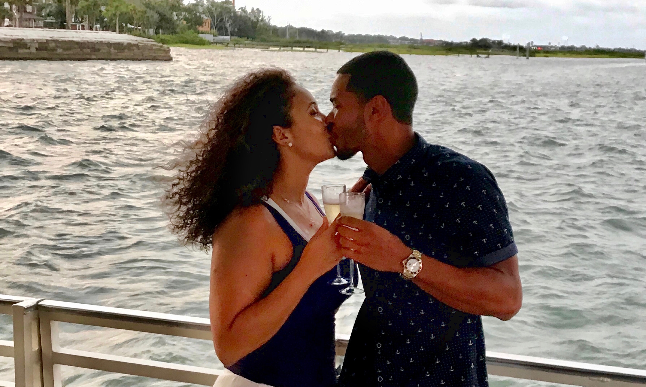 A couple, each holding a glass of sparkling wine, kiss on the deck of a Red Boat Water Tours