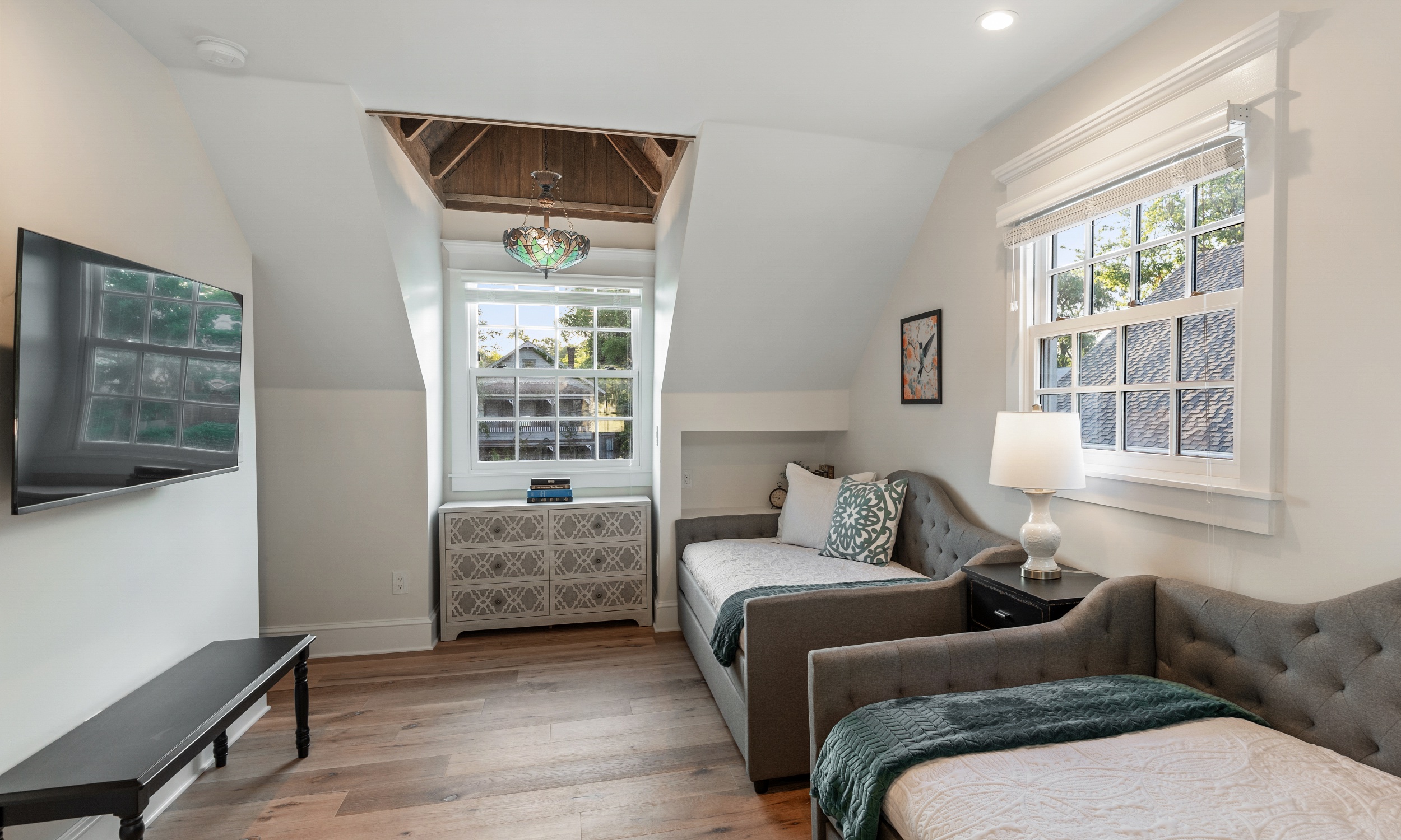 A small bedroom with twin beds that can be used as seating, and a television on the wall