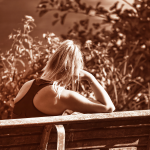 A sepia-toned image of a woman on a bench from behind. She leans her head on her hand as if in distress.