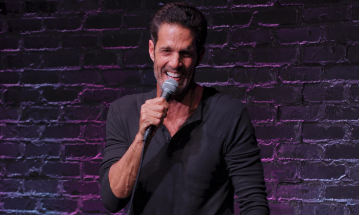 Pete Correale stands smiling as he speaks in front of a purple, brick-textured backdrop.